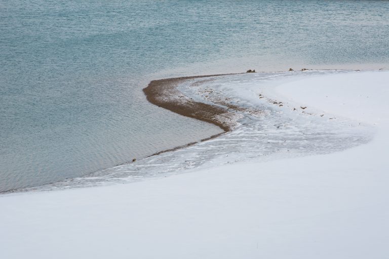 Photographie minimaliste d’un lac enneigé avec une rive courbe et un grand espace négatif de neige