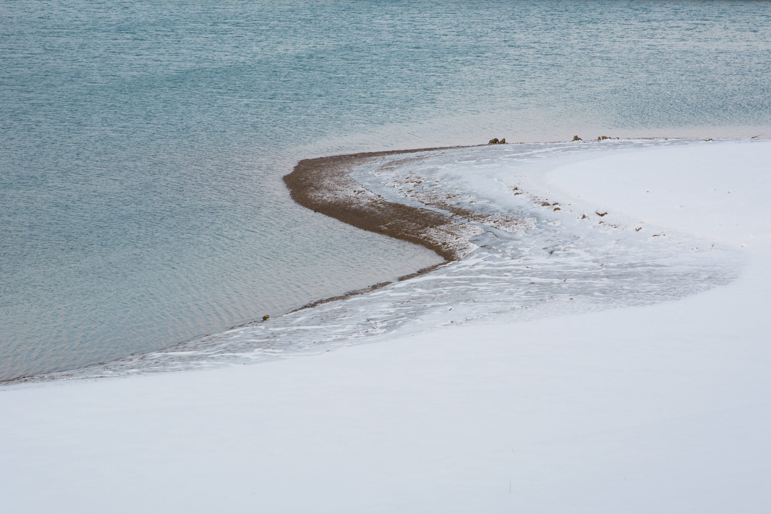 Photographie minimaliste d’un lac enneigé avec une rive courbe et un grand espace négatif de neige
