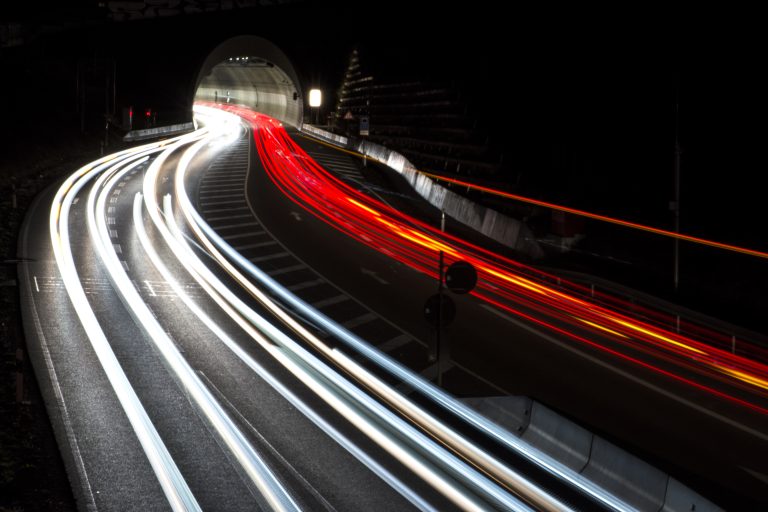 Pose longue photo de nuit : filés de phares rouges et blancs sur une route vers un tunnel