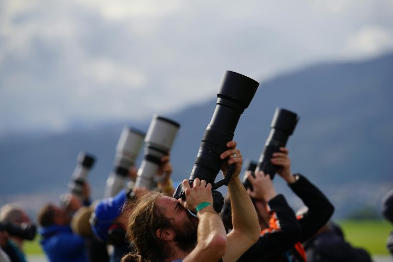 Photographes levant de longs téléobjectifs vers le ciel en extérieur, avec montagnes floues en arrière-plan