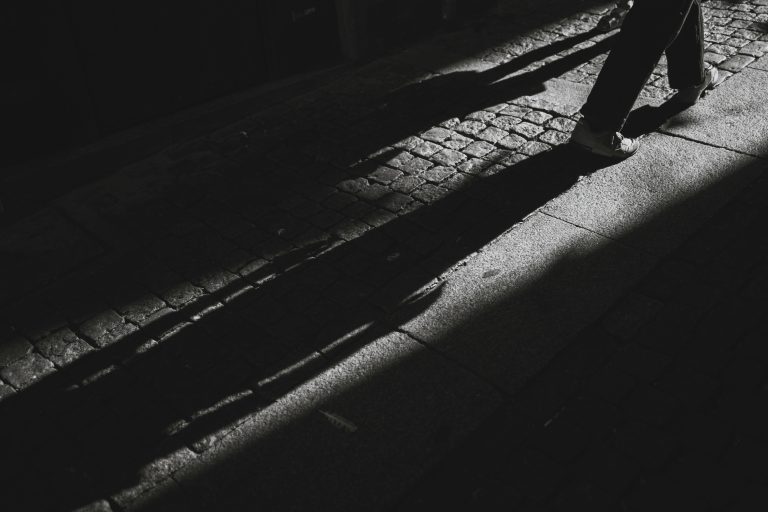 Ombres longues d’un passant sur une rue pavée en noir et blanc