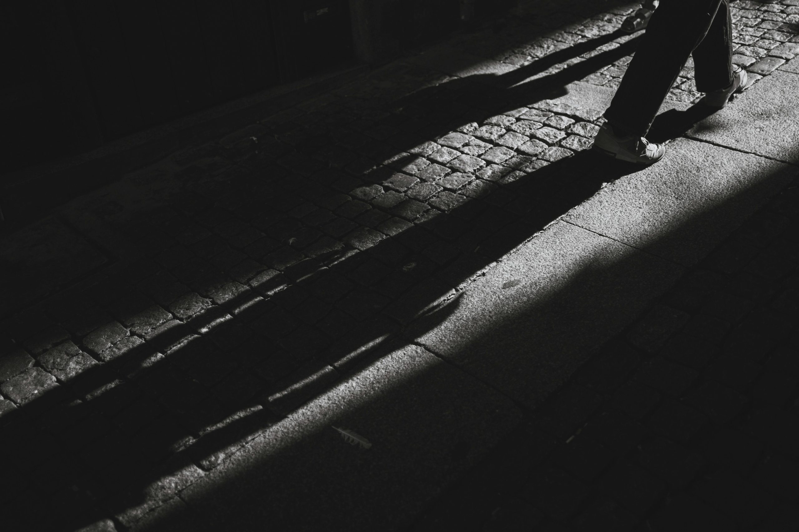 Ombres longues d’un passant sur une rue pavée en noir et blanc