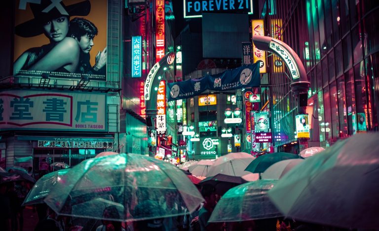 Foule sous des parapluies dans le quartier de Shibuya à Tokyo, sous les enseignes lumineuses et la pluie