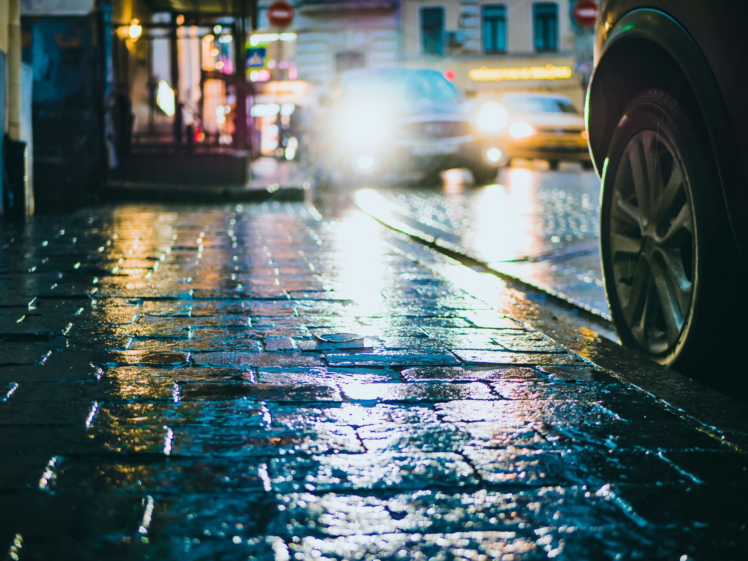 Reflets de phares et de lumières urbaines sur une rue pavée mouillée par la pluie