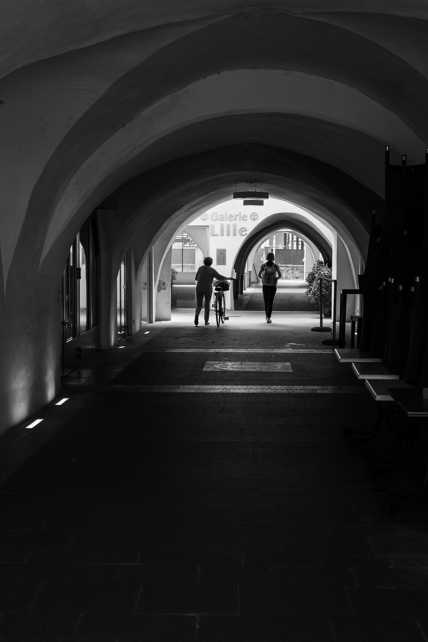 Silhouettes sous les arches de Vipiteno en street photo noir et blanc